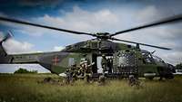 Mehrere Soldaten hocken und liegen vor einem NH-90-Hubschrauber, der Offizier befehligt seine Soldaten.