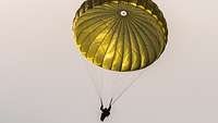 Ein Fallschirmjäger hängt an seinem gelb-grünen Fallschirm unter dem Himmel.