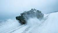 Auf einer verschneiten Straße fährt ein Panzer zügig.