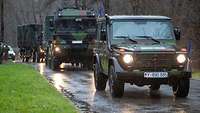 Mehrere Fahrzeuge der Bundeswehr unterwegs auf einer regennassen Straße.