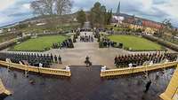 Vor einem Schloss im Hofgarten stehen zahlreiche Soldaten vor Gästen in Formation.