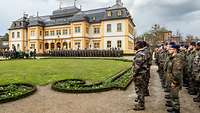 Vor einem Schloss im Hofgarten stehen zahlreiche Soldaten vor Gästen in Formation.