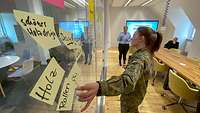 Eine Soldatin heftet Post-It's an eine Glaswand.