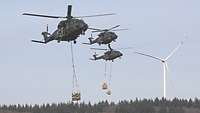 Drei Hubschrauber mit Außenlasten fliegen auf gleicher Höhe nebeneinander.