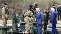 Zwei Zivilisten in blauen Anzügen schütteln jeweils einem Soldaten die Hand.