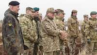 Neun Soldaten in unterschiedlichen Tarnuniformen stehen im Gras und blicken in eine Richtung.