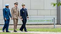 Drei Offiziere aus verschiedenen Nationen gehen vor einem Gebäude entlang und unterhalten sich.
