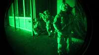 Fallschirmjägerregiment beim Training bei Dunkelheit Blick durch ein Nachtsichtgerät in Grün: Soldaten stehen mit ihren Waffen an einem Haus in Stellung