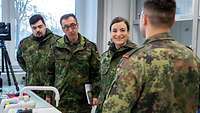 Alt: Drei Menschen in Uniform hören einer anderen Person in Uniform zu