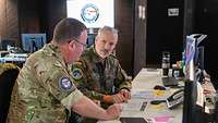 Ein deutscher und ein britischer Soldat sitzen an einem Tisch und besprechen etwas.
