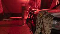 Drei Soldaten sitzen unter einer roten Lampe, im Vordergrund hängt eine Jacke mit einem MAD-Aufnäher auf einem Geländewagen.