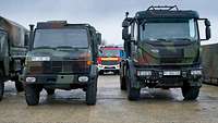2 Militärfahrzeuge, zwischen ihnen fällt der Blick auf ein ziviles Feuerwehrfahrzeug