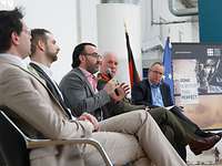 Panel II beim CSPD Mehrere Personen sitzen auf einer Bühne. Ein Mann spricht in ein Mikrofon.