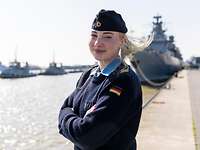 Eine Frau steht an einer Pier. Hinter ihr ist ein Schiff zu erkennen.
