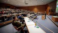 Blick in einen Konferenzsaal mit zahlreichen Soldaten und Politikern. Ein Soldat steht vorn am Pult.