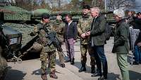 Drei Soldaten und drei Zivilisten sprechen vor Militärfahrzeugen miteinander.