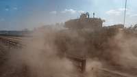 Ein Panzer fährt schnell einen trockenen Geländeweg entlang. Sand wirbelt auf.