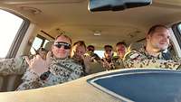 Fünf Soldaten und eine Soldatin sitzen gemeinsam im Fahrzeug und lächeln in die Kamera.