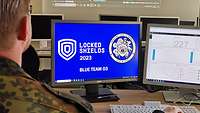 Zwei Männer sitzen vor zwei Monitoren mit der Inschrift Locked Shields 2023 Blue Team 03.
