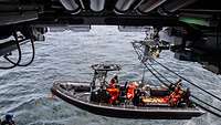 Ein Schlauchboot mit Soldaten hängt an einer Aussetzvorrichtung und wird zu Wasser gelassen