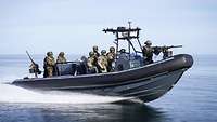Mehrere Soldaten fahren in einem Schlauchboot mit Festrumpf auf einem Gewässer