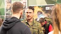 Ein Soldat spricht mit einem Besucher. Hinter dem Soldaten ein Poster mit Aufschrift KSK.
