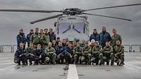 27 Personen haben sich vor einem Hubschrauber platziert.