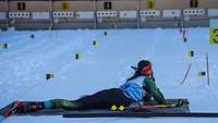Eine Biathletin liegt auf der Matte und zielt auf die Scheiben im Hintergrund.