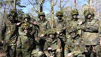 Eine Gruppe junger Menschen in Uniform mit Tarnung. Sie blicken die Betrachtenden an.