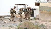 Vier Soldaten eilen in Sturmtruppformation zu einem Gebäude.