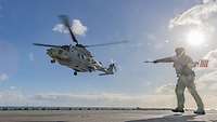 An aircraft handler is guiding a helicopter in landing approach.