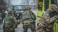 Deutsche, Briten und Esten trainieren auf der Ämari Air Base Ein estnischer, ein britischer und ein deutscher Soldat suchen Deckung hinter einem Feuerwehrfahrzeug