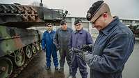Vier Soldaten in Arbeitsoveralls stehen neben einem Kampfpanzer Leopard. Einer bedient ein Gerät.
