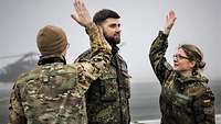 Eine deutsche Soldatin und ein US-Soldat schlagen einem deutschen Soldaten auf die Schulterklappen.
