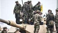 Zahlreiche deutsche und US-Soldaten stehen auf einem Kampfpanzer und unterhalten sich.