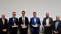 Sechs Männer stehen nebeneinander und lächeln in die Kamera.