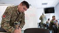 A soldier writing on a sheet of paper.