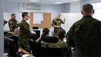 A soldier in front of a flip chart is talking to other soldiers.