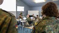A soldier in front of a flipchart ist talking to other soldiers.