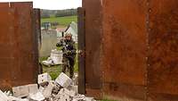 Ein Soldat mit Waffe läuft auf einen gesprengten Steinhaufen zu, links und rechts davon Metallwände.