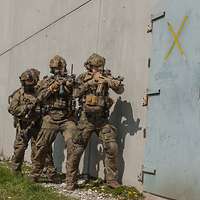 Vier Soldaten stehen mit Waffen im Anschlag vor einer hellblauen Stahltür.