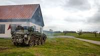 Waffenträger Wiesel Ein Kettenfahrzeug mit einer Bormaschinenkanone steht neben einem Haus.
