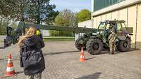 Junge Frau sitzt mit Hörschutz in Bundeswehrfahrzeug, daneben ein Soldat, eine weitere Frau wartet