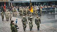 Drei deutsche Soldaten marschieren mit der deutschen Truppenfahne auf einem Platz in Tallinn
