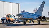 Ein deutsches Schleppfahrzeu zieht einen britischen Eurofighter vor der Wartungshalle in Ämari