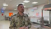 Ein Soldat steht vor der Ausgabe einer Kantine und spricht mit einer Interviewerin (nicht im Bild).