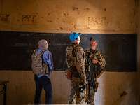 Besichtigung der Unterrichtsräume Zwei Soldaten und ihr Sprachmittler stehen in einem Klassenraum.