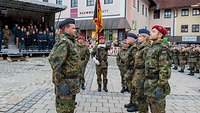 Soldatinnen und Soldaten an der Truppenfahne, im Hintergrund die Tribüne und Gäste