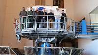 Seven persons are standing on a platform.