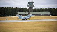 Ein Eurofighter hebt von der Startbahn ab, im Hintergrund sind der Tower und zwei Baracken zu sehen 